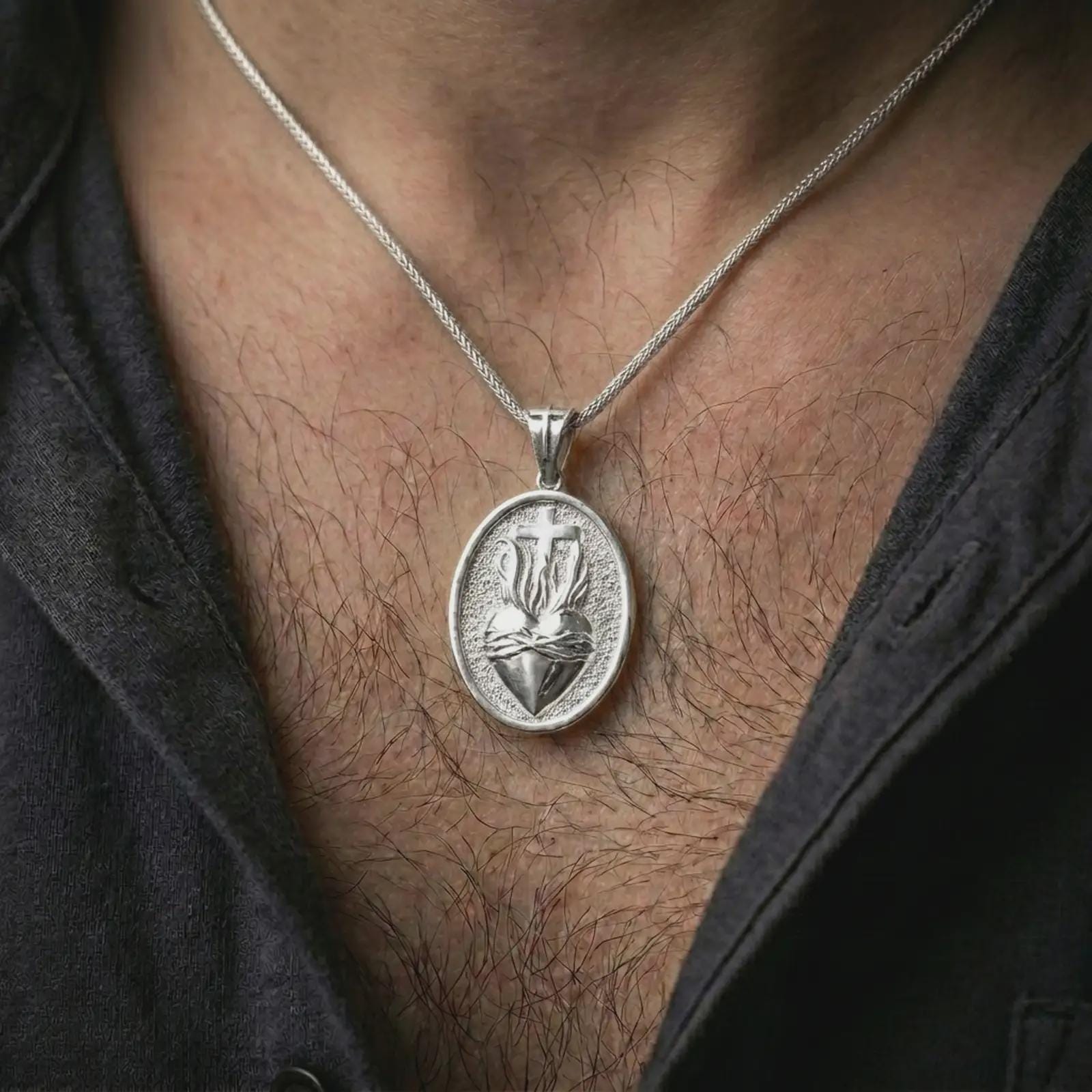 Polished silver Sacred Heart pendant necklace worn on the chest, masculine lifestyle shot highlighting the flaming heart relief, cross detail, and bright silver finish.