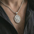 Load image into Gallery viewer, Polished silver Saint George pendant necklace worn on the chest, masculine lifestyle shot highlighting the mounted saint relief, spear, dragon detail, and bright silver finish.
