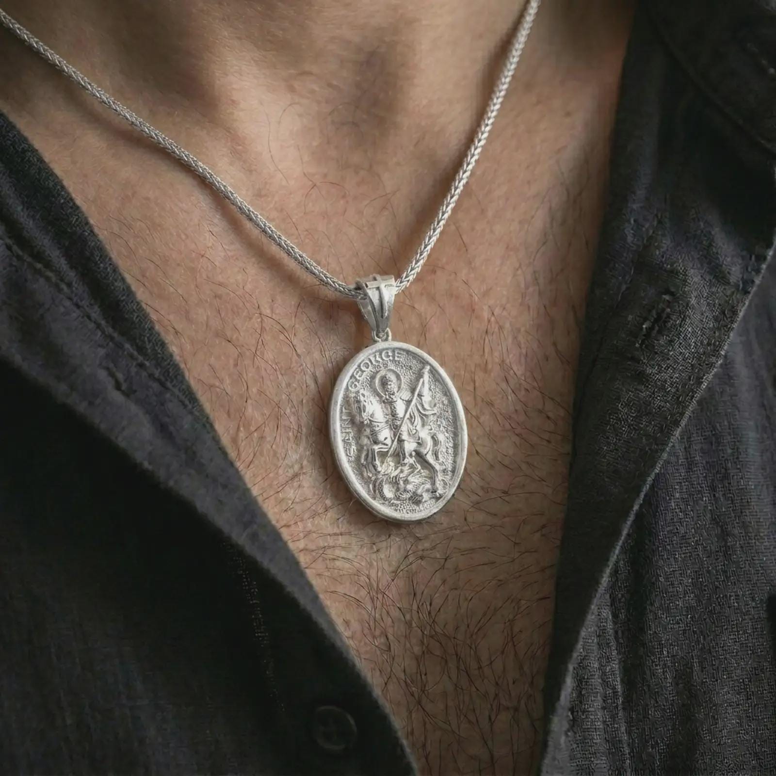 Polished silver Saint George pendant necklace worn on the chest, masculine lifestyle shot highlighting the mounted saint relief, spear, dragon detail, and bright silver finish.