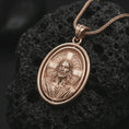 Load image into Gallery viewer, Rose gold plated spinning Jesus Christ pendant necklace on textured volcanic rock, detailed macro product shot with soft warm reflections and sacred Christian symbolism.
