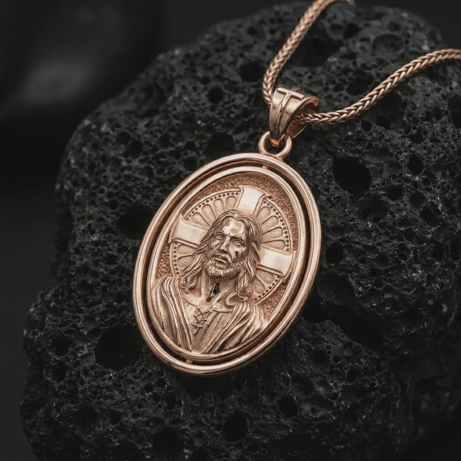 Rose gold plated spinning Jesus Christ pendant necklace on textured volcanic rock, detailed macro product shot with soft warm reflections and sacred Christian symbolism.