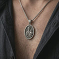 Load image into Gallery viewer, Oxidized Saint Joseph and Jesus pendant necklace worn on the chest, close-up lifestyle jewelry photo showing the Catholic medallion on a spiga chain with dark clothing.
