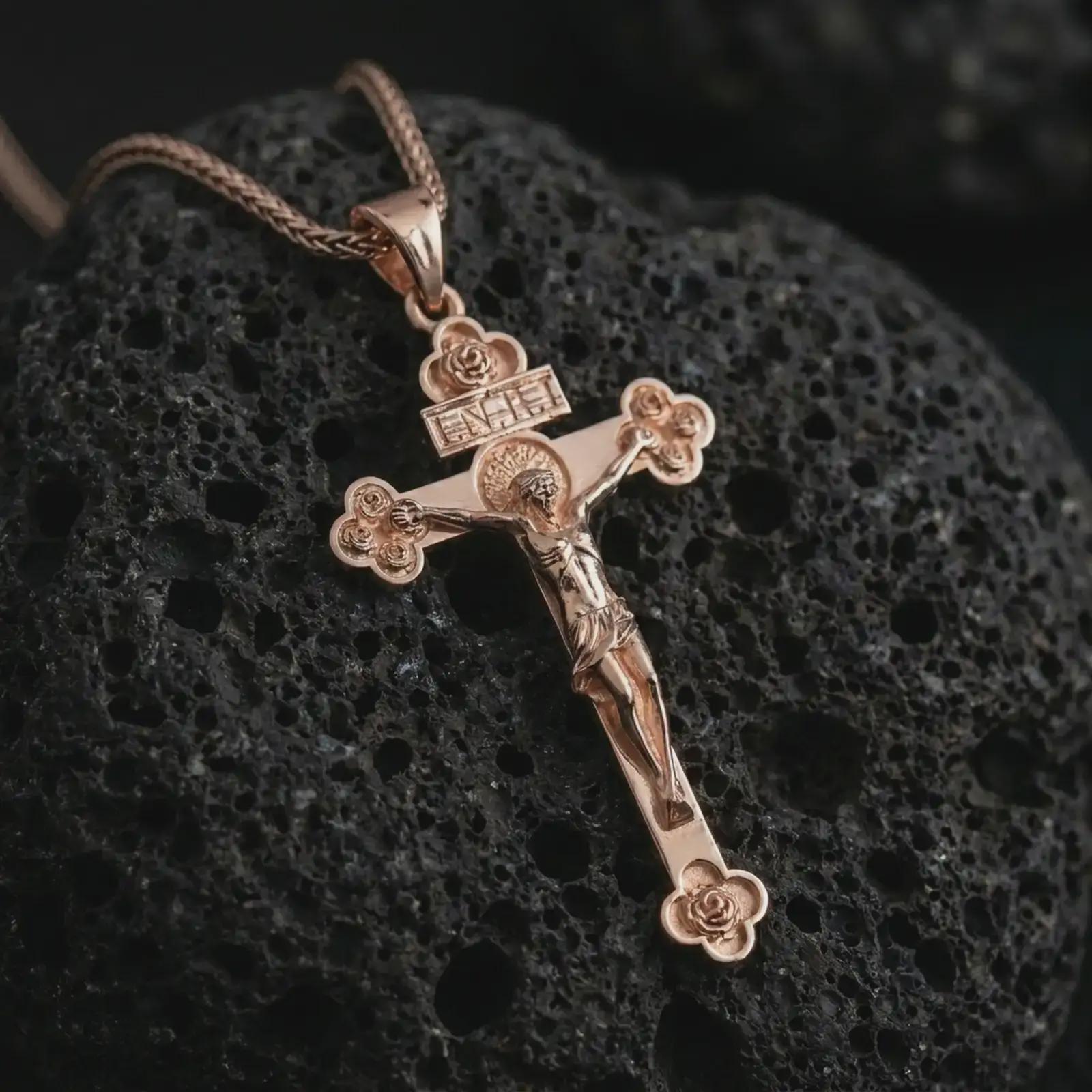 Rose gold plated crucifix pendant necklace on porous black volcanic rock, featured in a detailed macro image with the crucified Christ figure and elegant ornamental accents.