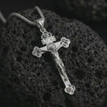 Load image into Gallery viewer, Polished silver crucifix pendant necklace resting on textured volcanic rock, shown in a premium macro product shot that emphasizes the sacred cross design and refined religious detailing.
