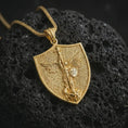 Load image into Gallery viewer, Gold plated Saint Michael pendant necklace presented on textured black volcanic stone, showcasing the warrior angel design and symbolic Christian protection details in a luxury macro shot.
