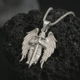 Load image into Gallery viewer, Polished silver angel warrior pendant necklace resting on dark volcanic rock, highlighting the armored celestial figure with spread wings and a strong protective stance.
