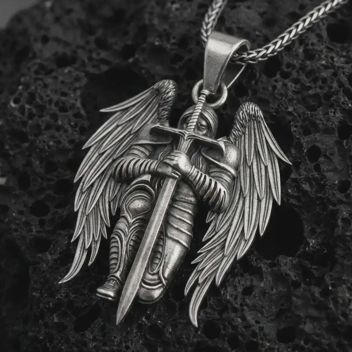 Oxidized angel warrior pendant necklace displayed on black volcanic stone, featuring a winged guardian holding a long sword in a bold and detailed sterling silver design.