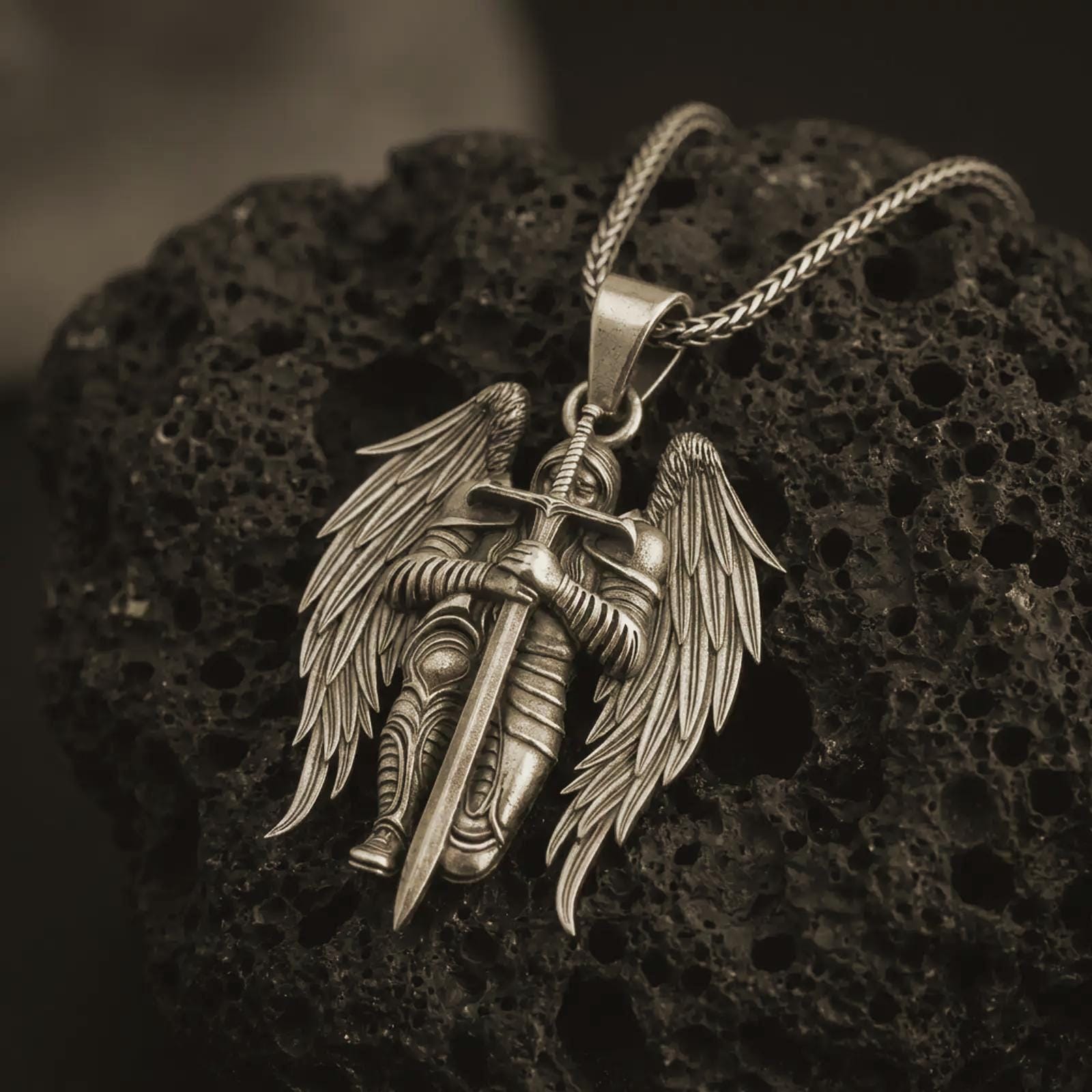 Bronze angel warrior pendant necklace displayed on black volcanic stone, featuring a winged guardian holding a long sword in a bold and detailed sterling silver design.