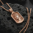 Load image into Gallery viewer, Rose gold plated INRI Jesus pendant necklace on textured volcanic rock, detailed macro product shot with soft warm reflections and sacred Christian symbolism.

