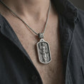Load image into Gallery viewer, Oxidized Saint Dominic dog tag pendant necklace worn on the chest, close-up lifestyle jewelry photo showing the religious medallion on a spiga chain with dark clothing.
