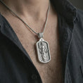 Load image into Gallery viewer, Polished silver Saint Dominic dog tag pendant necklace worn on the chest, masculine lifestyle shot highlighting the saint relief, book detail, lily, and bright silver finish.
