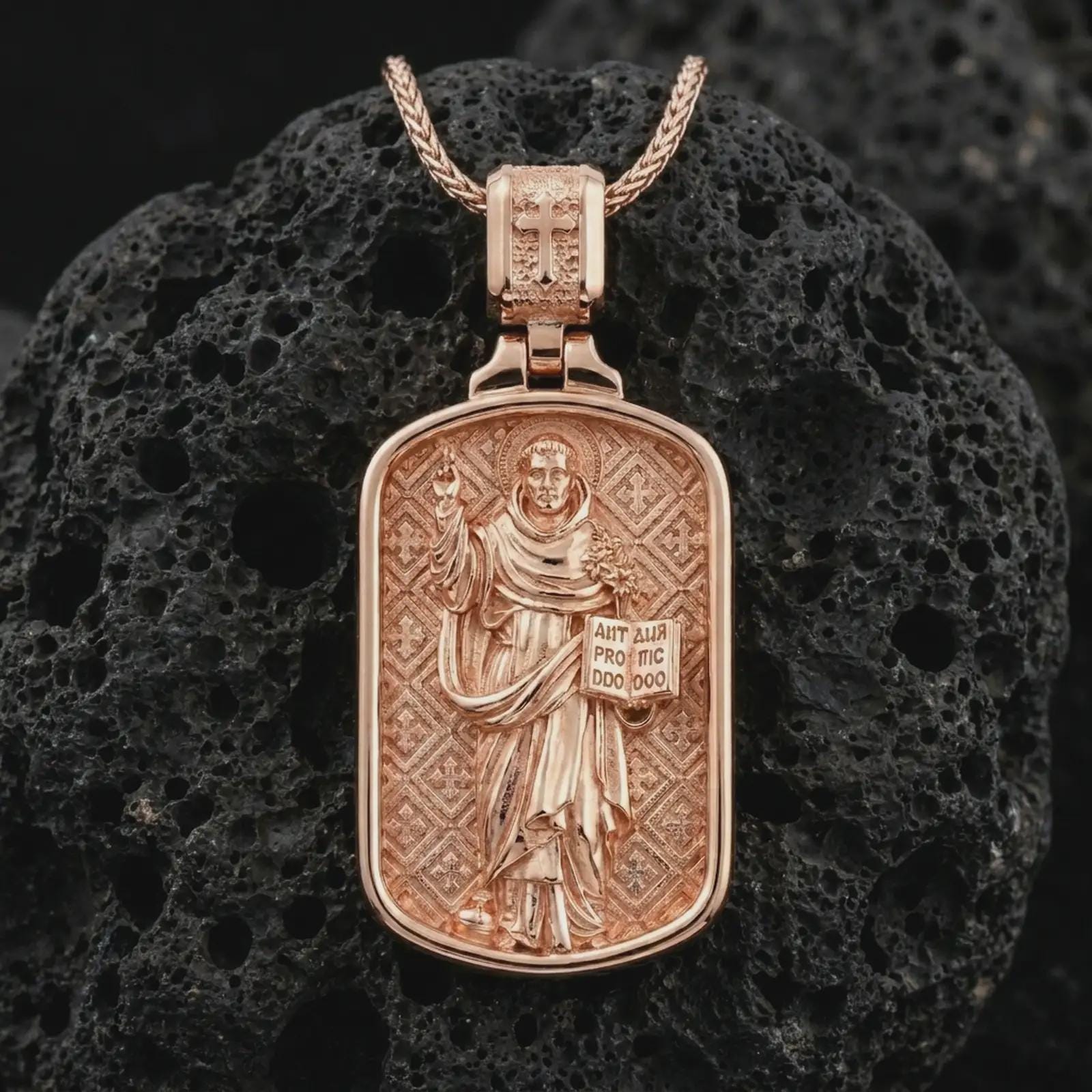 Rose gold plated Saint Dominic dog tag pendant necklace on textured volcanic rock, detailed macro product shot with soft warm reflections and devotional Saint Dominic design.