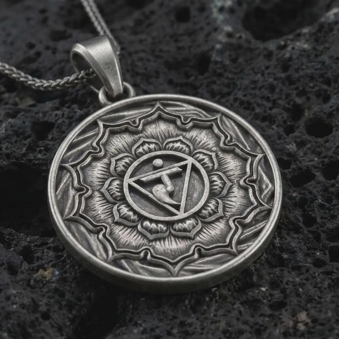 Oxidized Manipura chakra pendant necklace on textured volcanic rock, close-up studio shot highlighting the solar plexus symbol, lotus petals, geometric center, and antique silver contrast.