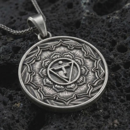 Oxidized Manipura chakra pendant necklace on textured volcanic rock, close-up studio shot highlighting the solar plexus symbol, lotus petals, geometric center, and antique silver contrast.