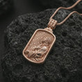 Load image into Gallery viewer, Rose gold plated Jesus prayer dog tag pendant necklace on textured volcanic rock, detailed macro product shot with soft warm reflections and devotional Christ symbolism.
