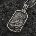 Load image into Gallery viewer, Oxidized Jesus prayer dog tag pendant necklace on textured volcanic rock, close-up studio shot highlighting the side-profile Christ relief, halo, prayer pose, and antique silver contrast.
