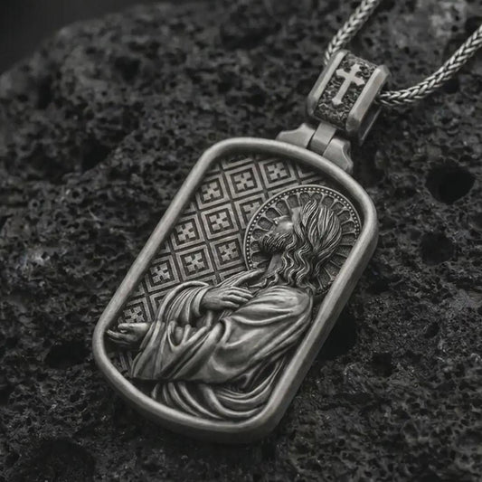 Oxidized Jesus prayer dog tag pendant necklace on textured volcanic rock, close-up studio shot highlighting the side-profile Christ relief, halo, prayer pose, and antique silver contrast.