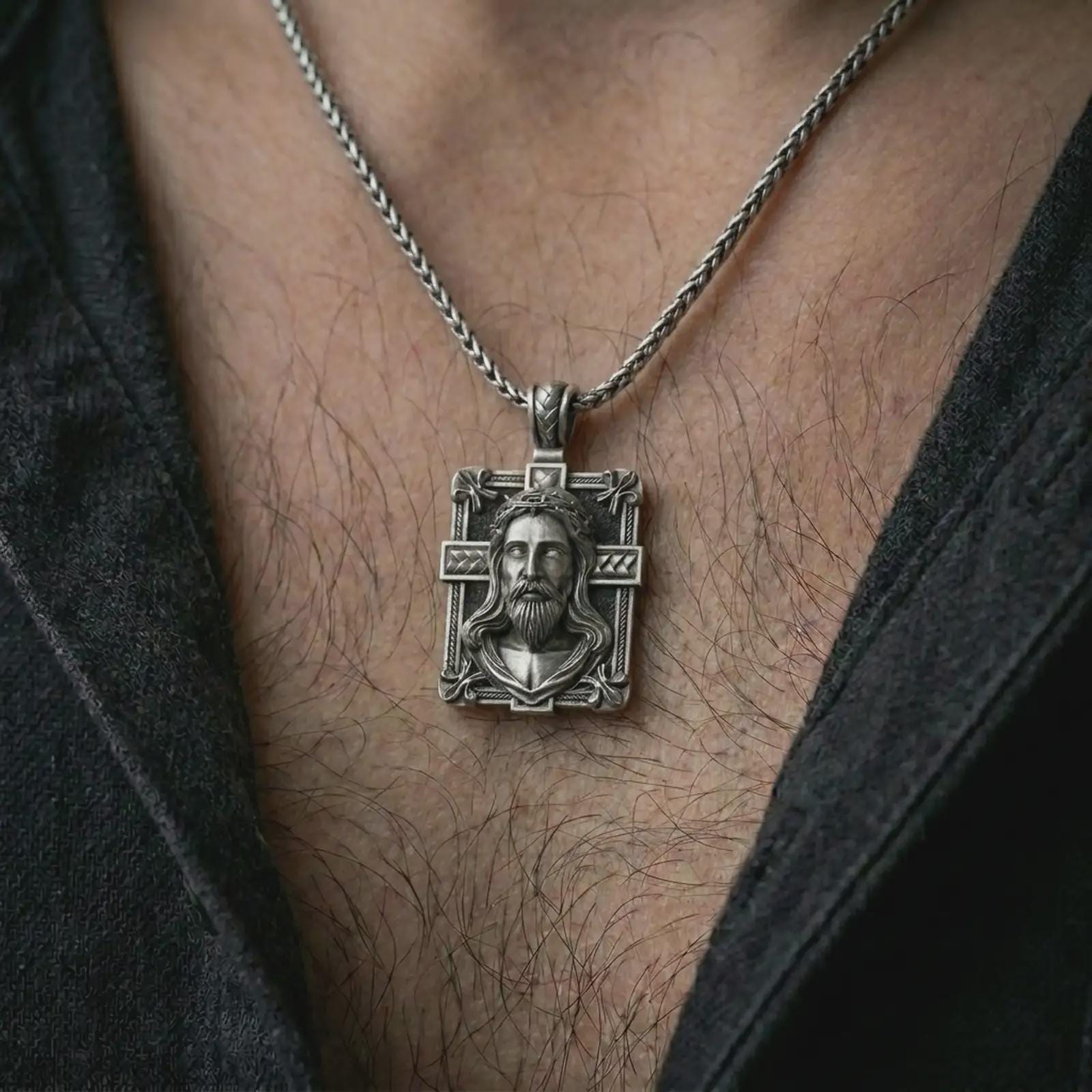 A Jesus crucifix pendant in an oxidized finish worn on the neck on a chain in a clean lifestyle close-up.