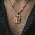 Load image into Gallery viewer, A Jesus crucifix pendant in a rose gold plated finish worn on the neck on a chain in a clean lifestyle close-up.
