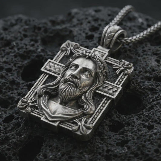 A Jesus crucifix pendant in an oxidized finish resting on porous volcanic rock in a premium macro studio shot.