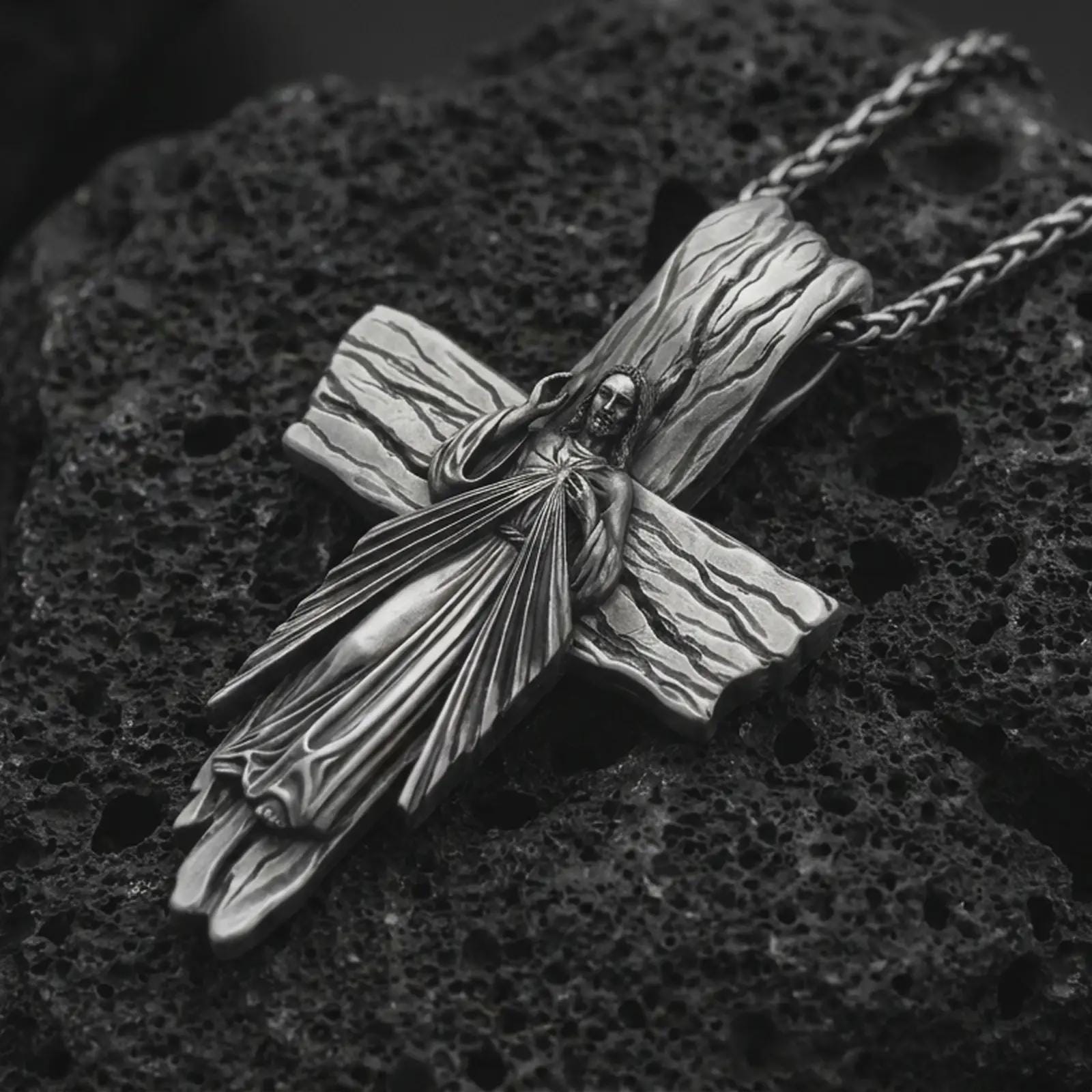 Oxidized Jesus cross pendant necklace on textured volcanic rock, close-up studio shot highlighting the Christ figure, radiant sacred heart, wood texture, and antique silver contrast.