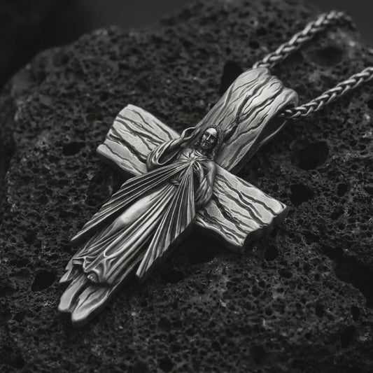 Oxidized Jesus cross pendant necklace on textured volcanic rock, close-up studio shot highlighting the Christ figure, radiant sacred heart, wood texture, and antique silver contrast.