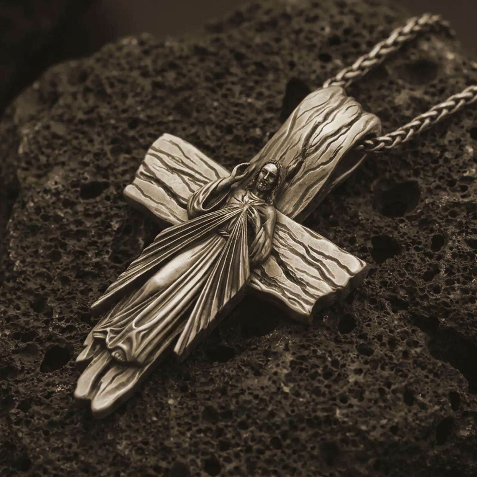 Bronze Jesus cross pendant necklace on textured volcanic rock, close-up studio shot highlighting the Christ figure, radiant sacred heart, wood texture, and antique silver contrast.