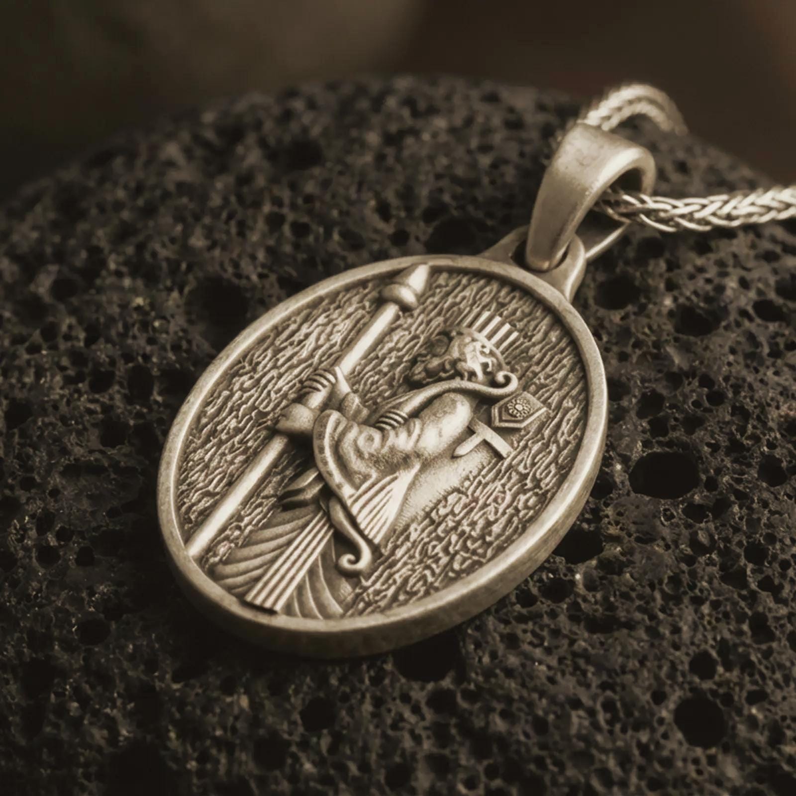 Bronze Achaemenid soldier pendant necklace with an oxidized finish resting on textured volcanic rock, captured in a close-up premium studio composition with a spear-bearing Persian warrior in oval relief.