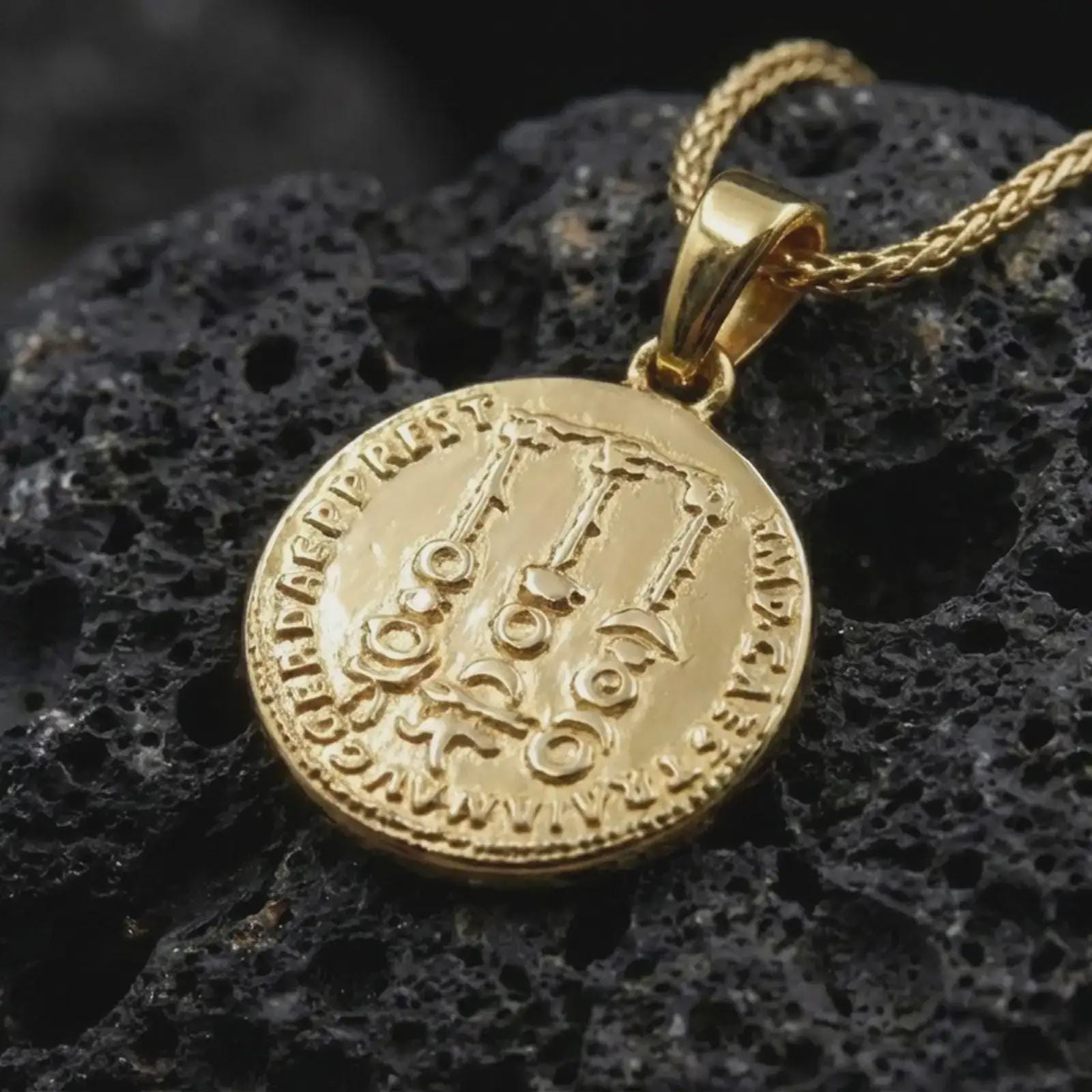 Gold plated Tiberius coin pendant necklace photographed on porous black volcanic stone, emphasizing the imperial side-profile relief and engraved ancient Roman lettering in a luxury jewelry composition.