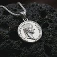 Load image into Gallery viewer, Polished silver Tiberius coin pendant necklace displayed on dark volcanic rock, shown in a premium close-up image that highlights the classical Roman portrait and historical coin medallion design.
