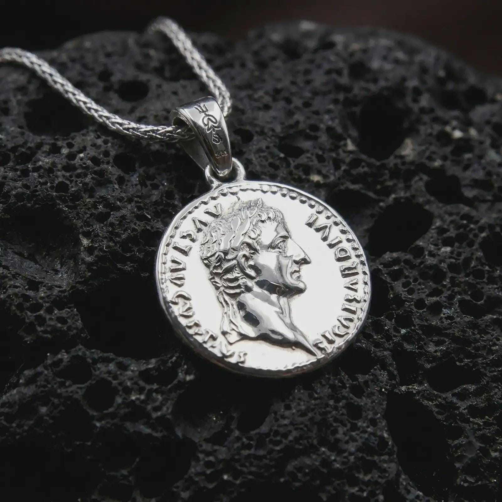 Polished silver Tiberius coin pendant necklace displayed on dark volcanic rock, shown in a premium close-up image that highlights the classical Roman portrait and historical coin medallion design.