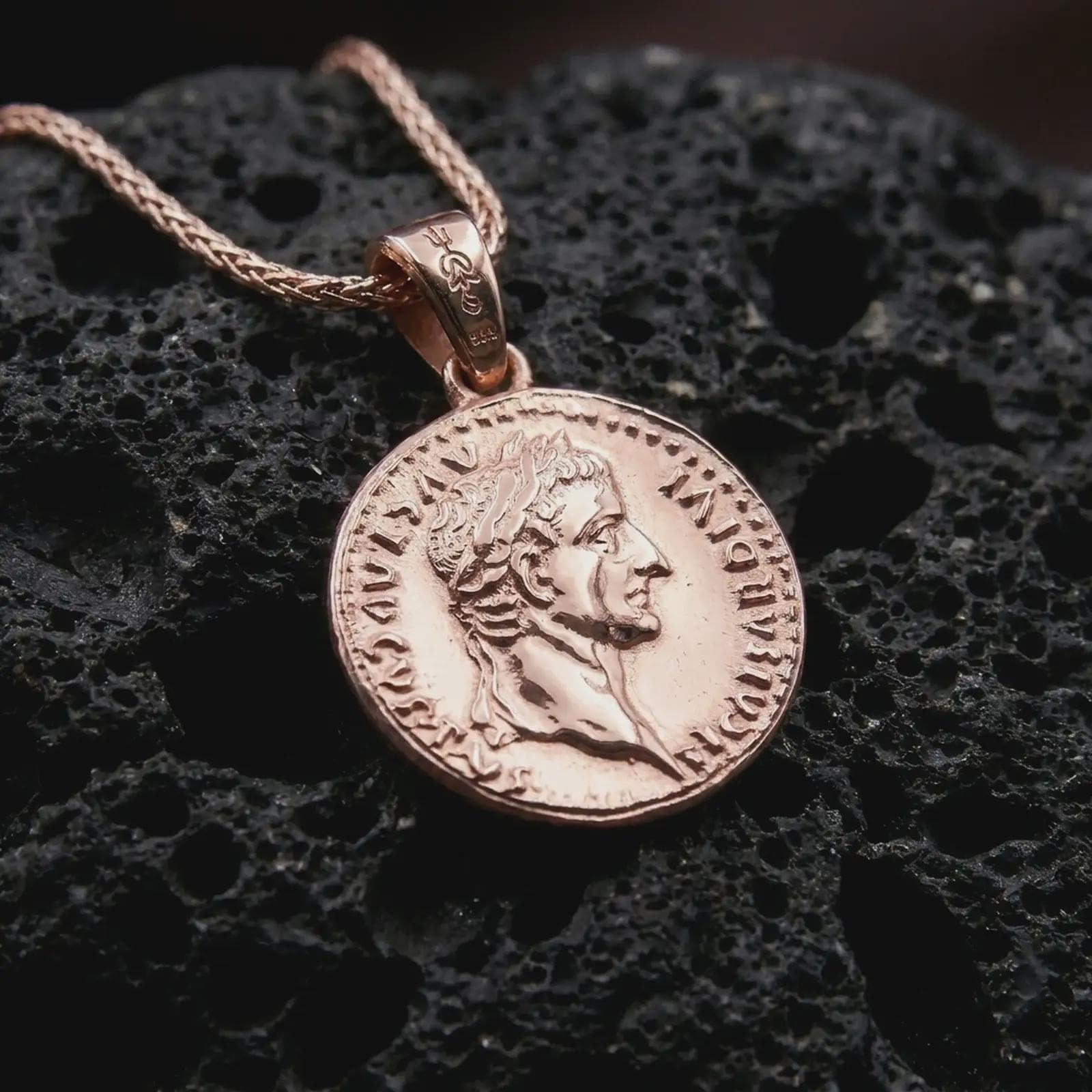 Rose gold plated Tiberius coin pendant necklace presented on textured volcanic stone, showcasing the round Roman coin silhouette and emperor bust in a refined macro studio shot.