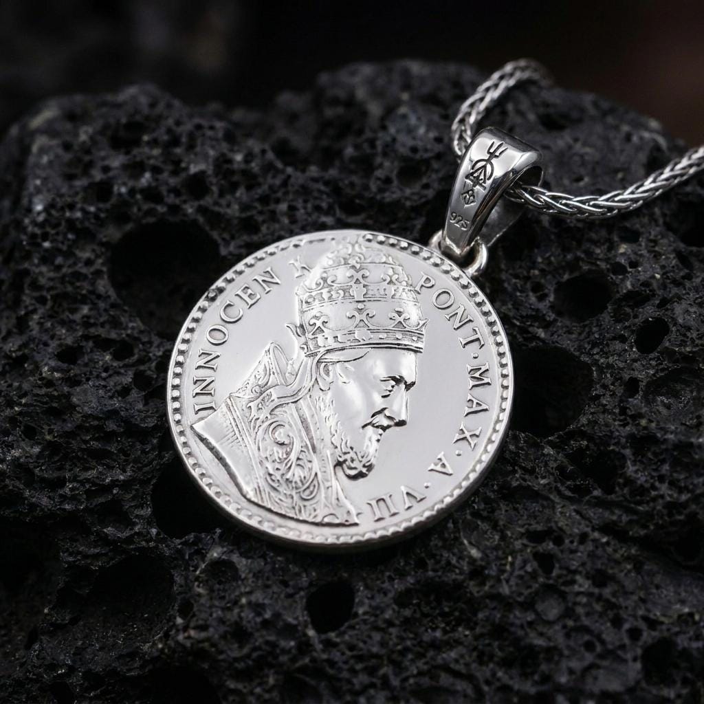 Polished silver Pope Innocent coin pendant necklace displayed on dark volcanic rock, shown in a premium close-up image that highlights the crowned papal bust and historical medal engraving.