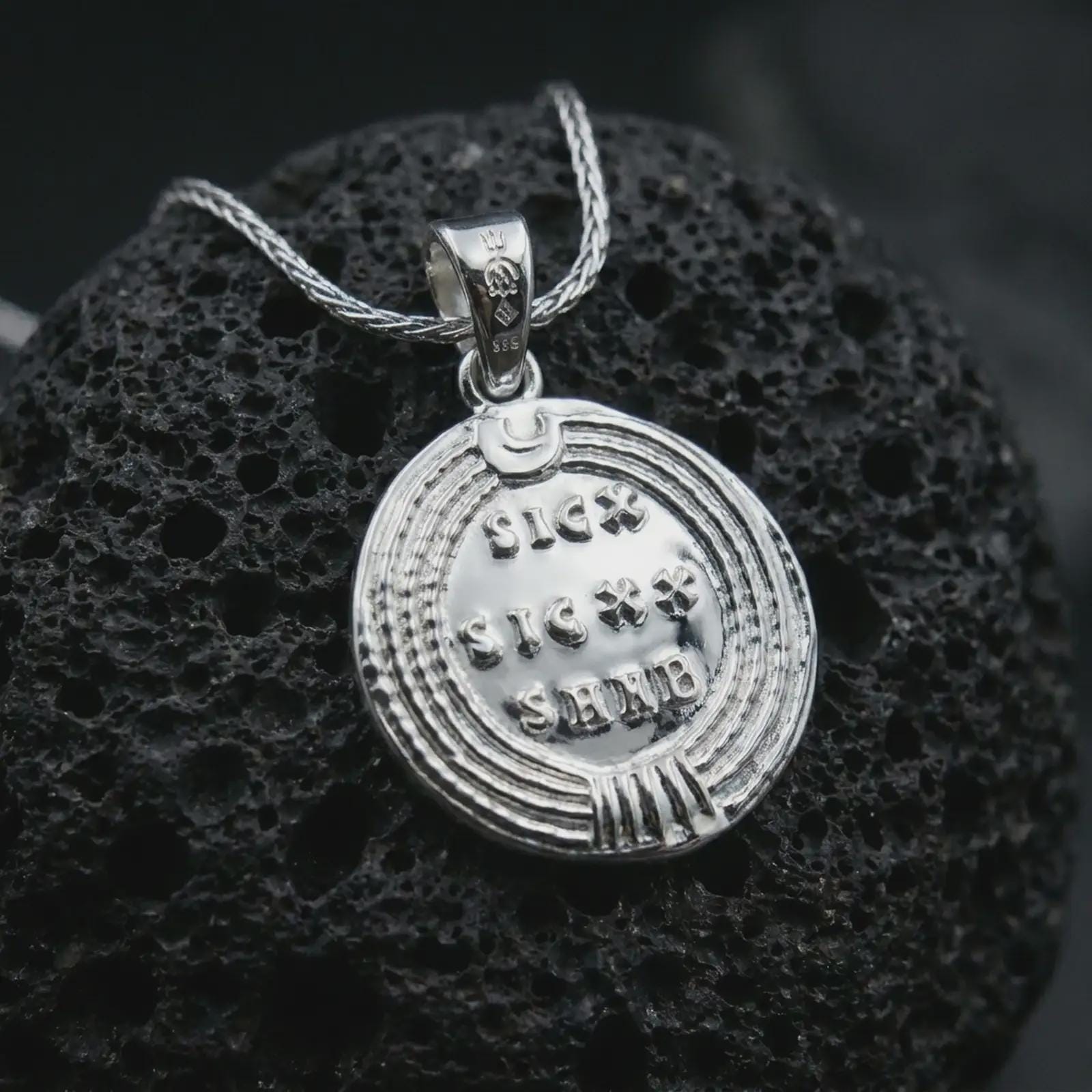 Polished silver Emperor Constans coin pendant necklace displayed on dark volcanic rock, shown in a premium close-up image that highlights the classical emperor portrait and ancient Roman coin texture.