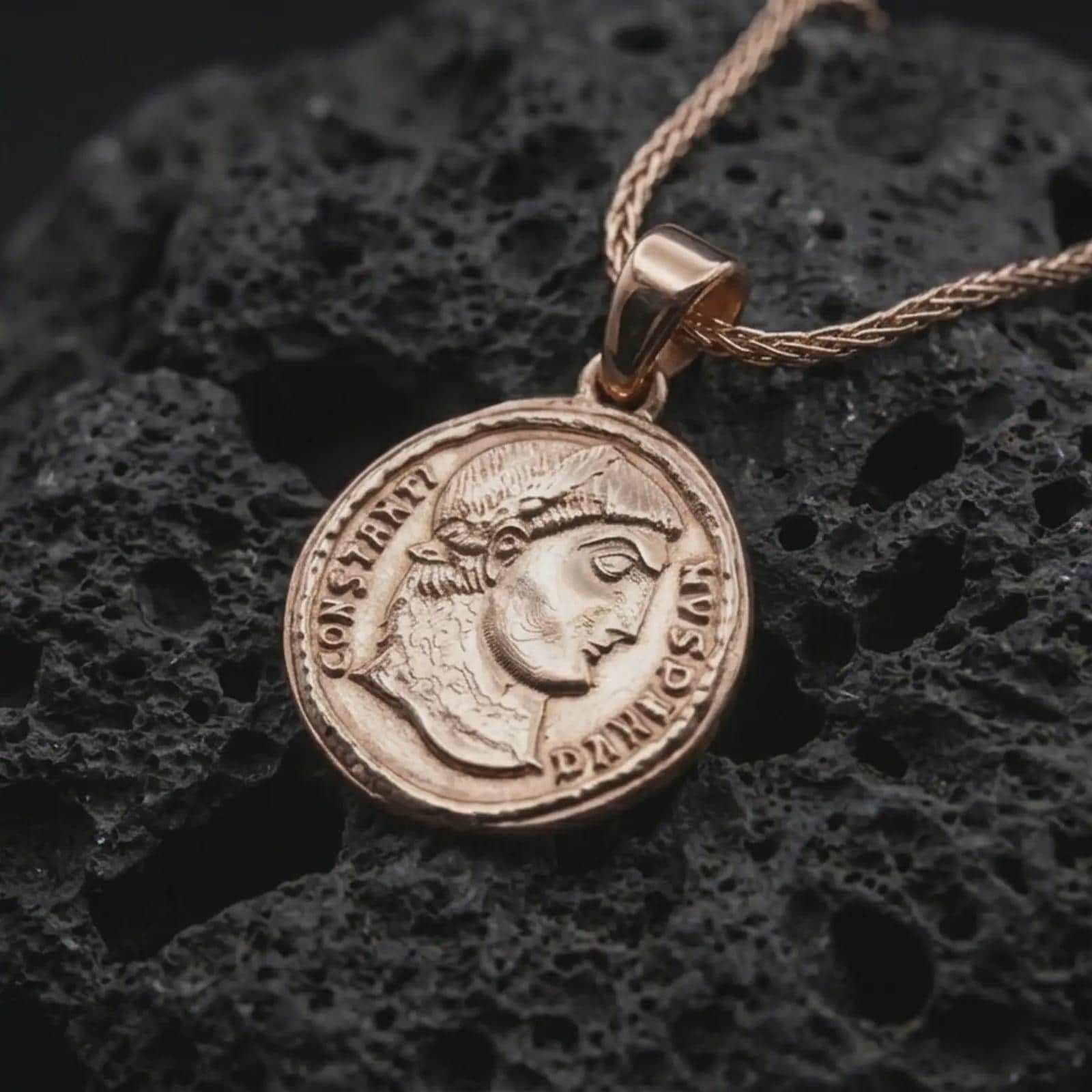 Rose gold plated Emperor Constans coin pendant necklace presented on textured volcanic stone, showcasing the round Roman coin silhouette and refined emperor relief in a macro studio shot.