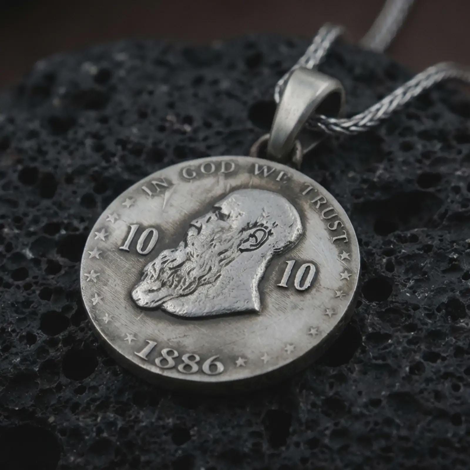 Oxidized heraldic eagle coin pendant necklace resting on black volcanic stone, featuring a round medallion with a crowned double-headed eagle, stars, and laurel branches in a detailed macro product photograph.