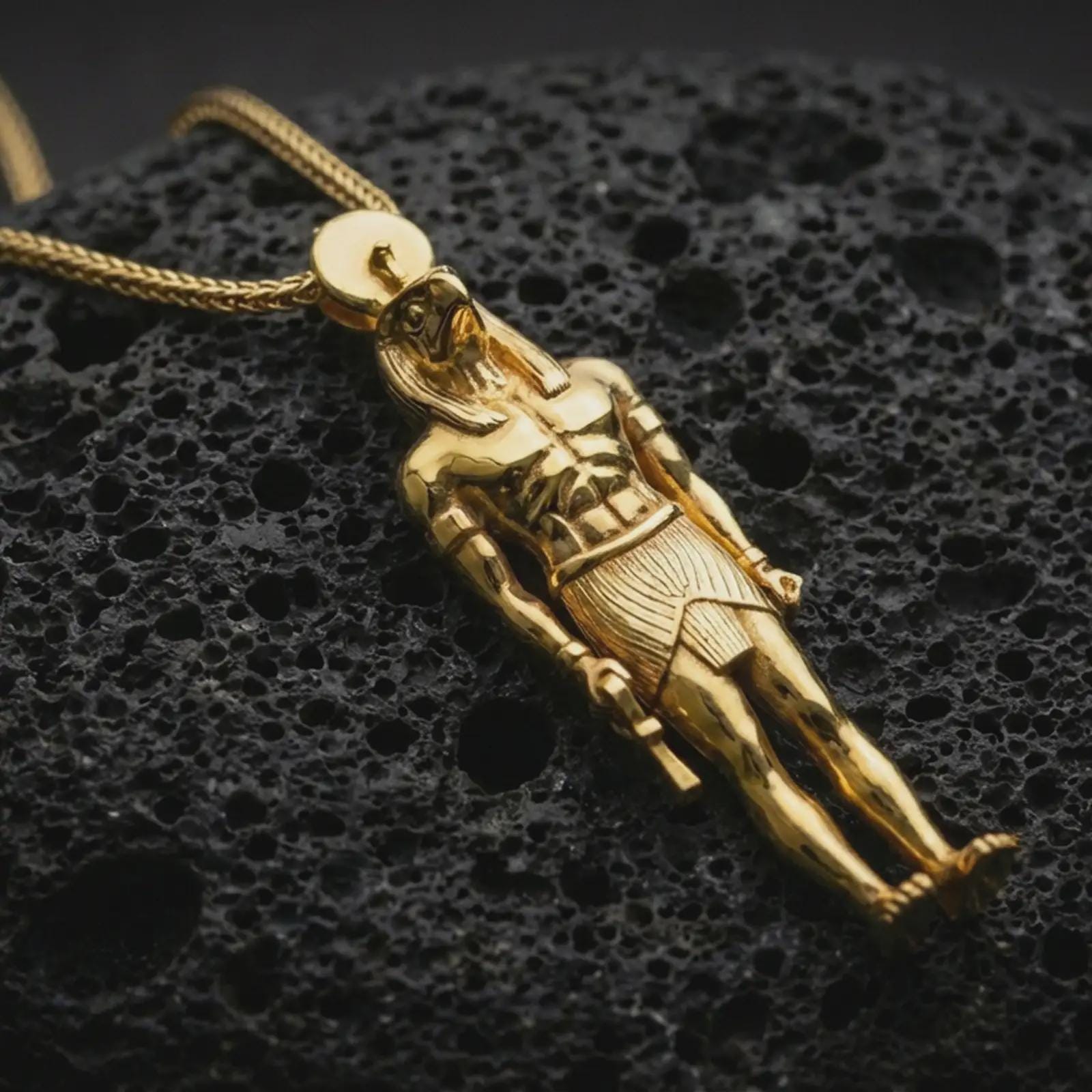 Gold plated Ra amulet pendant necklace photographed on porous black volcanic stone, emphasizing the ancient Egyptian sun god motif and refined historical detailing in a luxury jewelry composition.