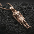Load image into Gallery viewer, Rose gold plated Ra amulet pendant necklace presented on textured volcanic stone, showcasing the standing deity form, iconic headpiece, and antique-inspired sacred design in a macro studio shot.
