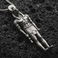 Load image into Gallery viewer, Oxidized Ra amulet pendant necklace resting on black volcanic stone, featuring an ancient Egyptian deity figure with a falcon-like head, sun disk, and strong sculpted body in a detailed macro product photograph.
