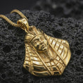 Load image into Gallery viewer, Gold plated Tutankhamun pendant necklace photographed on porous black volcanic stone, emphasizing the legendary king bust and historical Egyptian detailing in a luxury jewelry composition.
