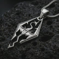 Load image into Gallery viewer, Polished silver Skyrim dragon pendant necklace on textured volcanic rock, centered macro jewelry photo with sharp fantasy emblem details and bright silver highlights.
