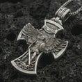 Load image into Gallery viewer, Oxidized Saint Michael cross pendant necklace on textured volcanic rock, close-up studio shot highlighting the archangel wings, sword, shield, demon detail, and antique silver contrast.
