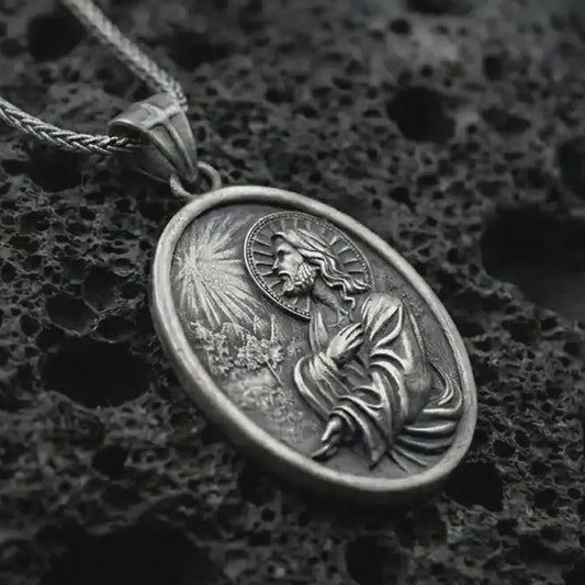 Oxidized Jesus Christ prayer pendant necklace on textured volcanic rock, close-up studio shot highlighting the praying Christ relief, radiant light detail, halo, and antique silver contrast.