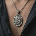 Load image into Gallery viewer, Oxidized Jesus Christ prayer pendant necklace worn on the chest, close-up lifestyle jewelry photo showing the religious medallion on a spiga chain with dark clothing.
