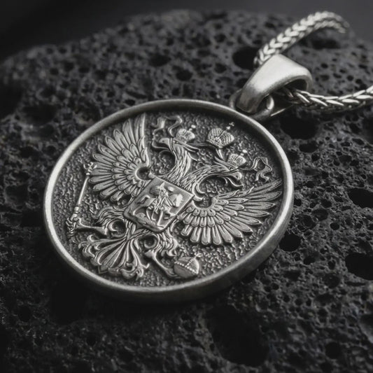 Oxidized double headed eagle pendant necklace resting on black volcanic stone, featuring a detailed heraldic eagle crest with spread wings and central shield in a macro product photograph.