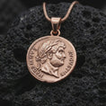 Load image into Gallery viewer, Rose gold plated Emperor Augustus coin pendant necklace presented on textured volcanic stone, showcasing the round Roman coin silhouette and refined emperor relief in a macro studio shot.
