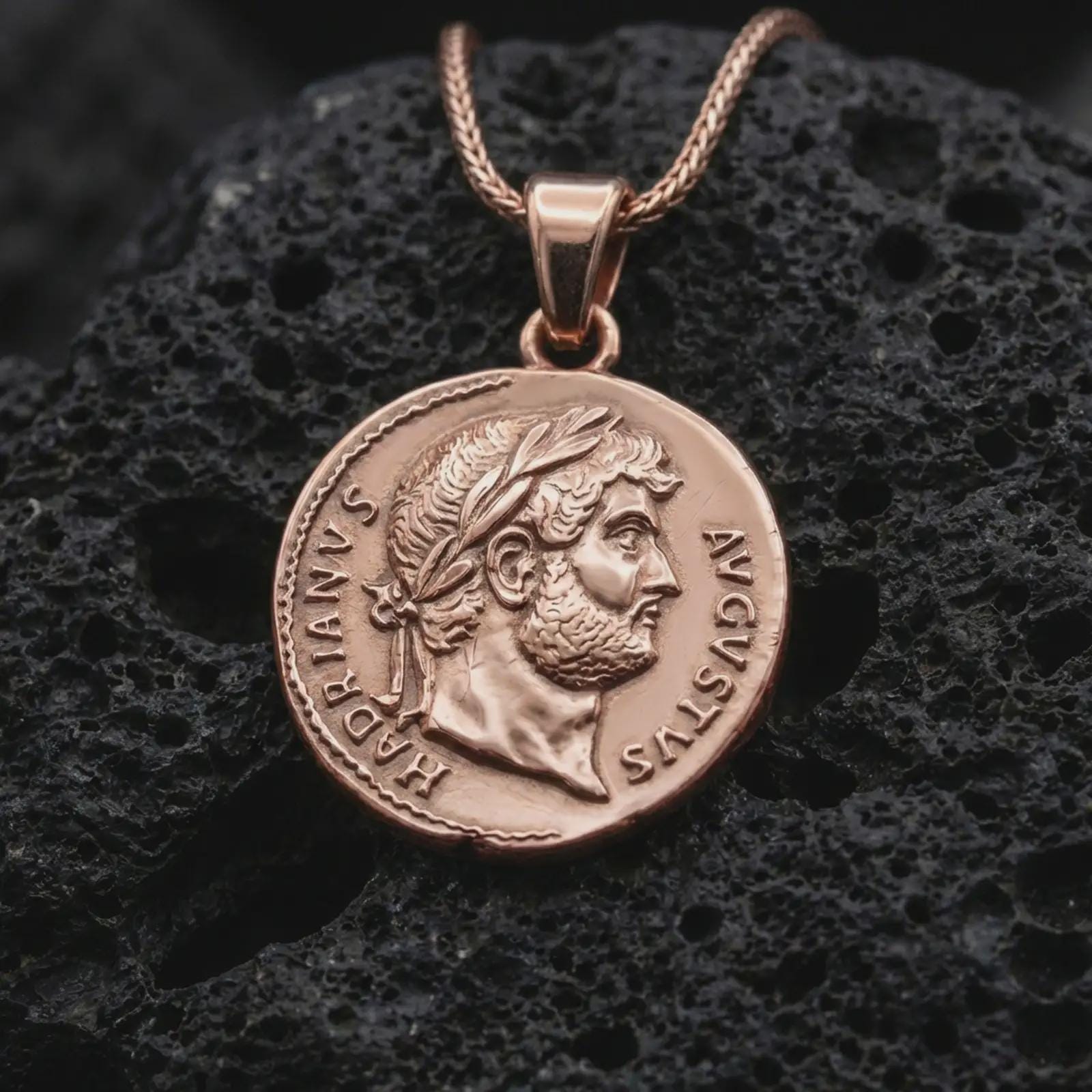 Rose gold plated Emperor Augustus coin pendant necklace presented on textured volcanic stone, showcasing the round Roman coin silhouette and refined emperor relief in a macro studio shot.