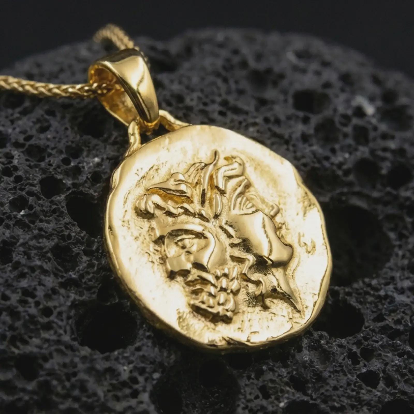 Gold plated Janus coin pendant necklace presented on porous black volcanic stone, photographed in a refined close-up image emphasizing the Roman god of beginnings and transitions in a coin-inspired design.