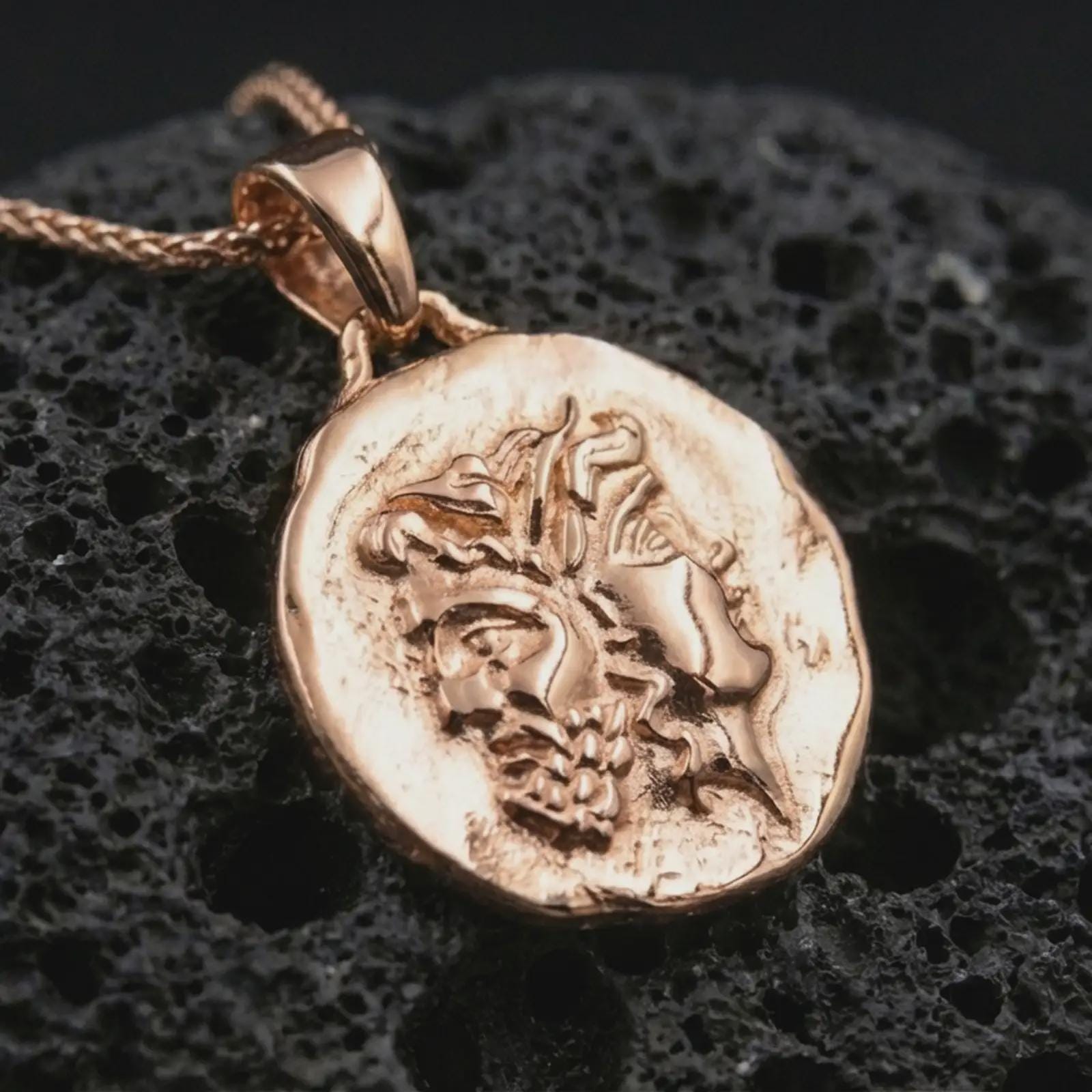 Rose gold plated Janus coin pendant necklace on textured volcanic rock, showcased in a luxury macro composition with the two-faced deity profile and irregular ancient coin form.
