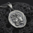 Load image into Gallery viewer, Oxidized Janus coin pendant necklace resting on black volcanic stone, featuring the ancient Roman two-faced god in a detailed antique-style relief and organic coin-shaped silhouette.
